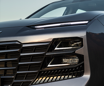 Close-up of a modern car's front grille and sleek LED headlights, showcasing a polished metallic finish and contemporary design elements.