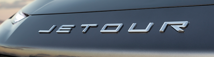 Close-up of the "JETOUR" emblem on a sleek car, highlighting its metallic lettering against a smooth, dark finish.