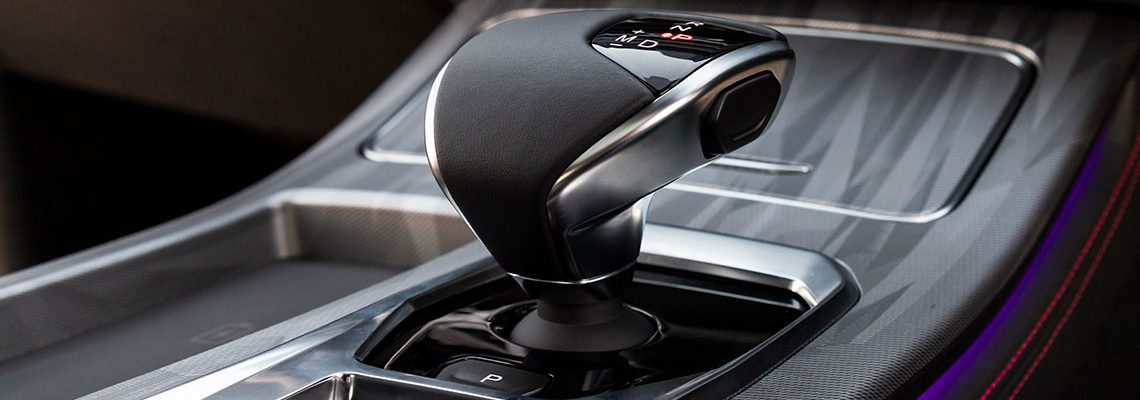 Close-up of a sleek car gear shift lever on a textured dashboard, showcasing modern design and illuminated gear indicators.