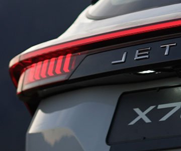 Close-up of a sleek white car's rear, featuring bold red taillights and "JET" lettering. The license plate reads "X7," conveying a modern, luxurious feel.
