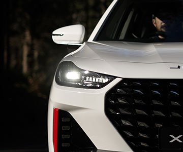 Close-up of a white SUV's front, showcasing LED headlights and a sleek grille design, set against a dark, blurred background, conveying a modern, powerful look.